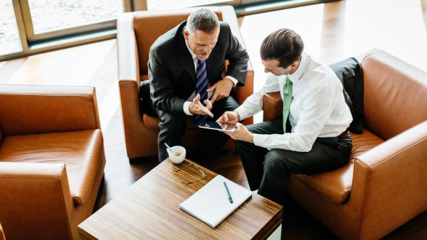Two Business Partners Looking At Digital Tablet Two business partners sitting down at the office looking at a digital tablet and reviewing documents.