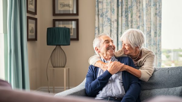 Senior couple hugging and having fun at home Happy senior woman embracing her husband at home while laughing together. Smiling wife hugging old man sitting on couch from behind. Joyful retired couple having fun at home while looking at each other with copy space. Love and unity concept.